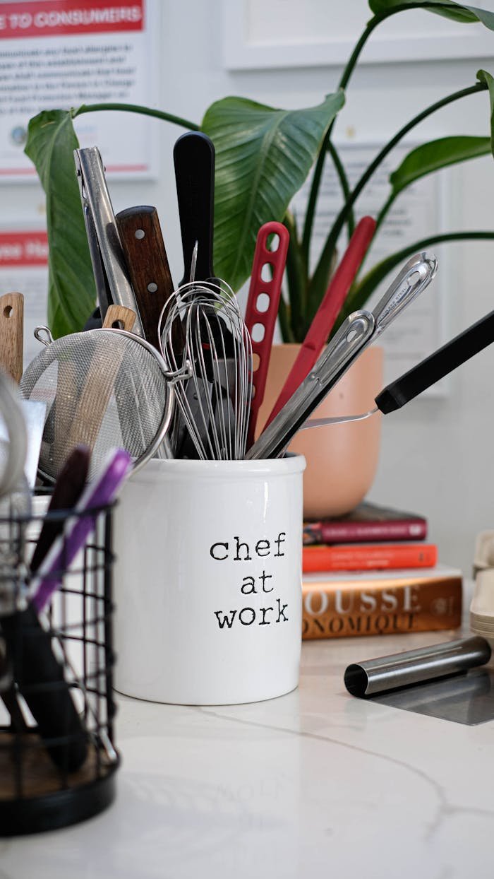 A collection of kitchen utensils in a 'Chef at Work' holder next to cookbooks.